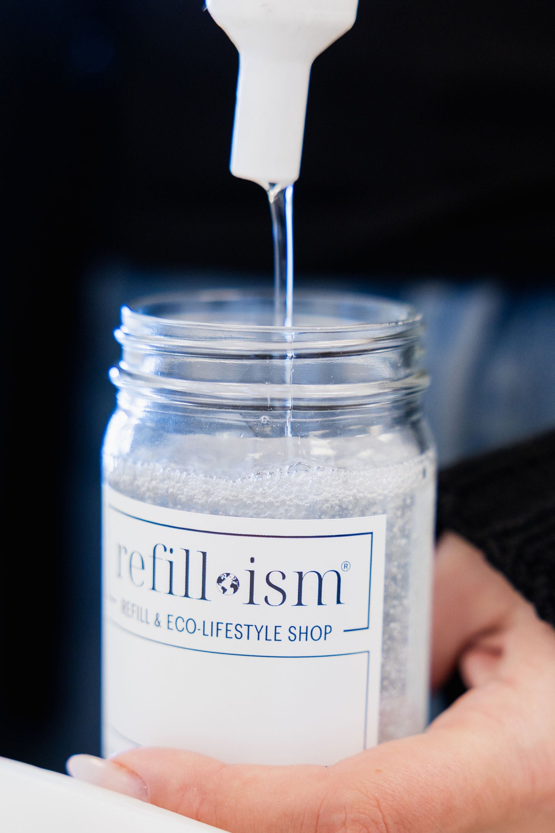 Person pouring liquid into a jar labeled 'refillism' with a blurred background.