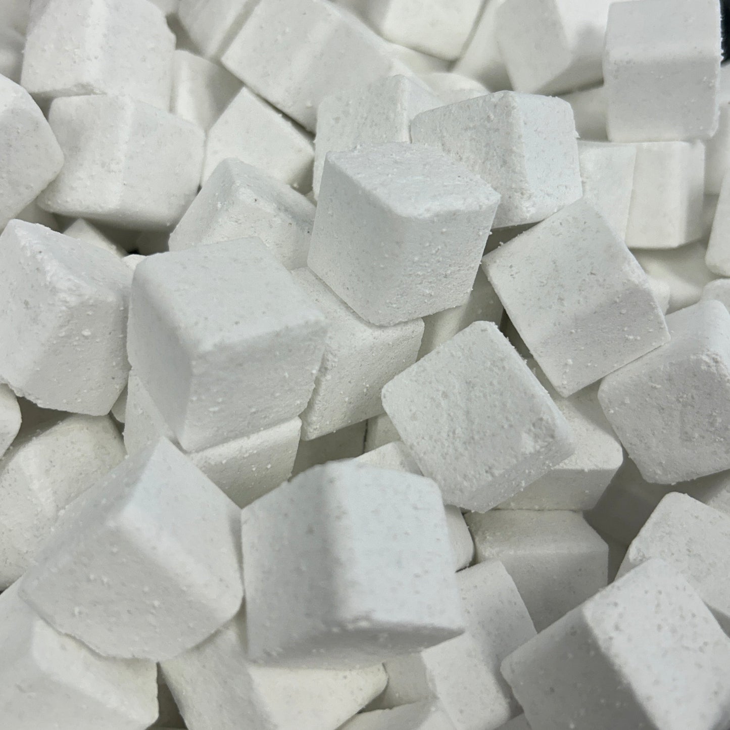 A close-up view of many small white cube-shaped blocks piled together in a clear plastic container.