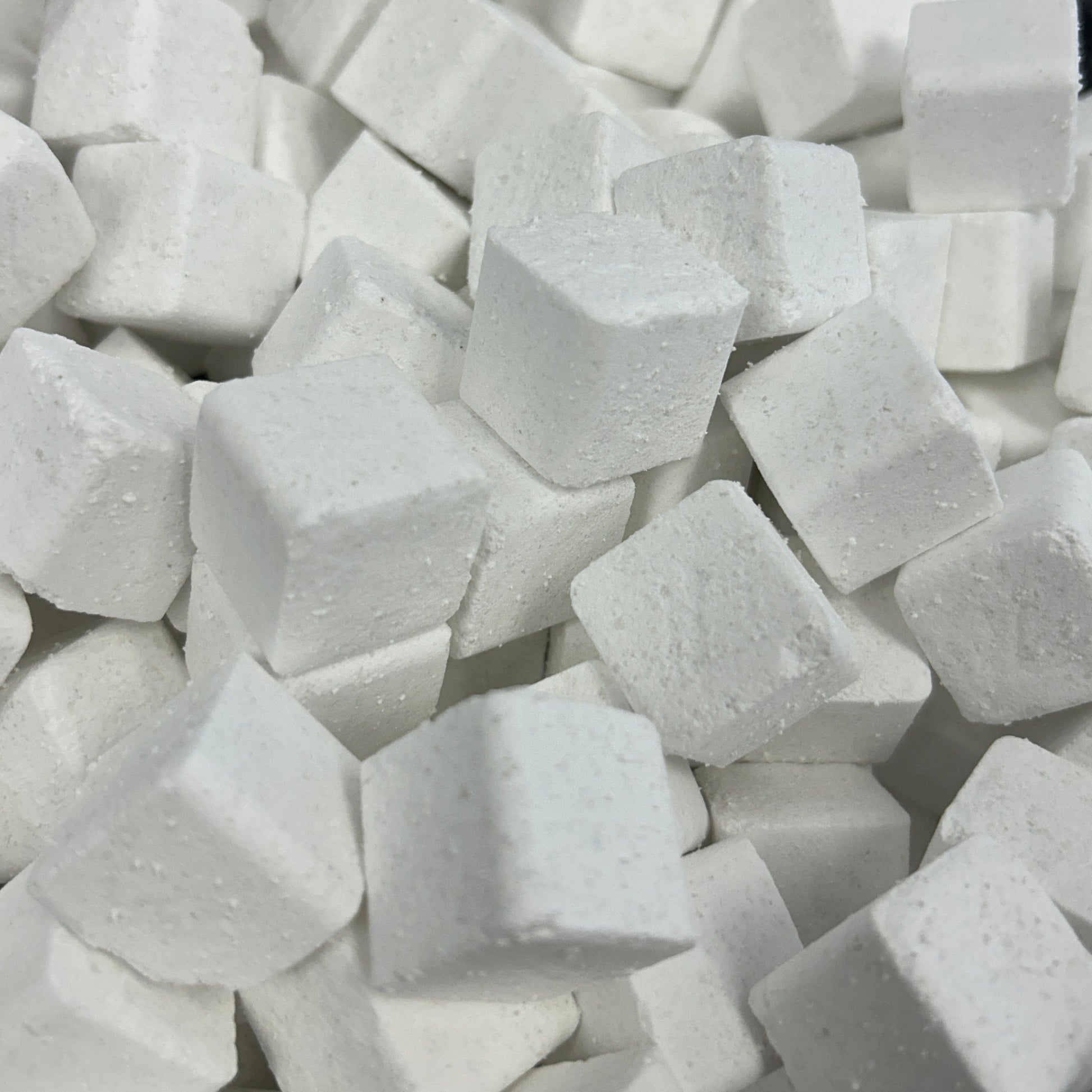 A close-up view of many small white cube-shaped blocks piled together in a clear plastic container.
