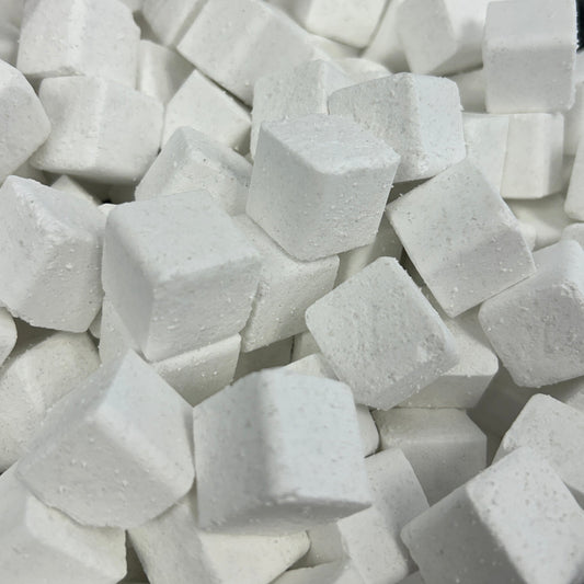 A close-up view of many small white cube-shaped blocks piled together in a clear plastic container.